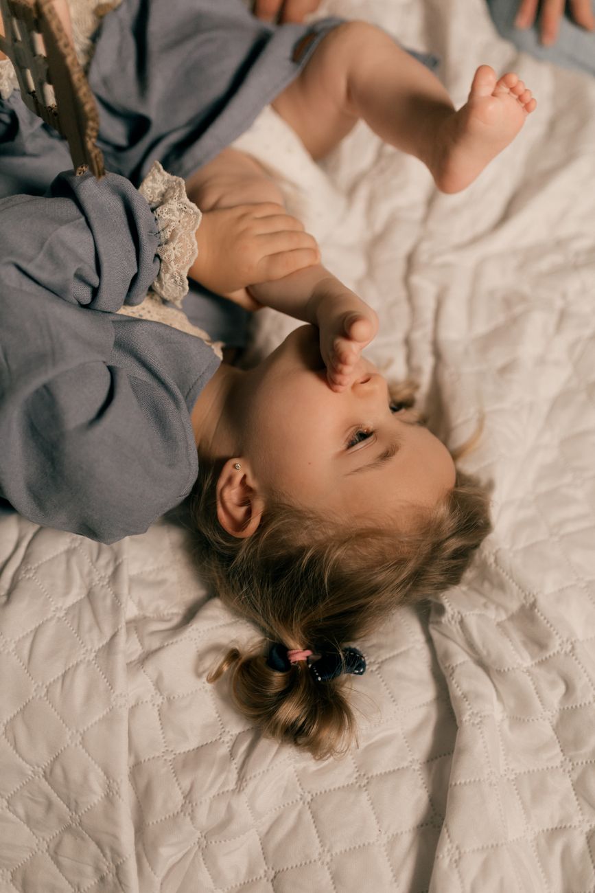 A toddler lying on a quilted bed sucking their thumb