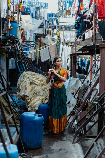 A woman in traditional saree stands at Mumbai's Dhobi Ghat amidst clothes and water tanks.