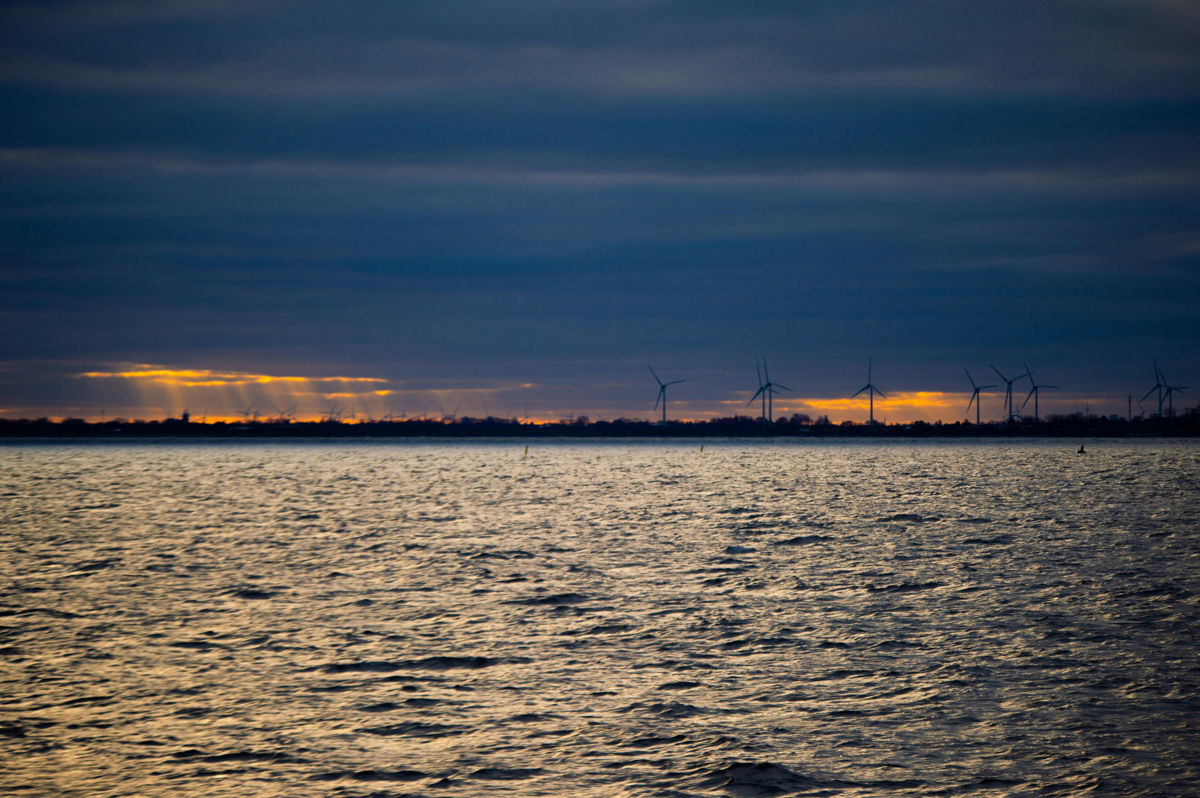 Captivating sunset over the water with wind turbines in the distance, showcasing sustainable energy and natural beauty.