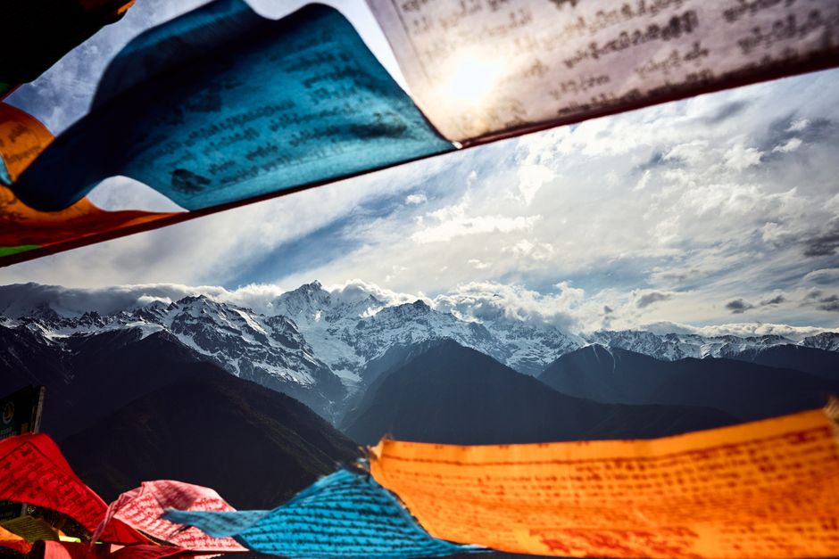 Panorama of the Tibetan Plateau with a string of prayer flags stretching across a high pass, snow peaks in the distance