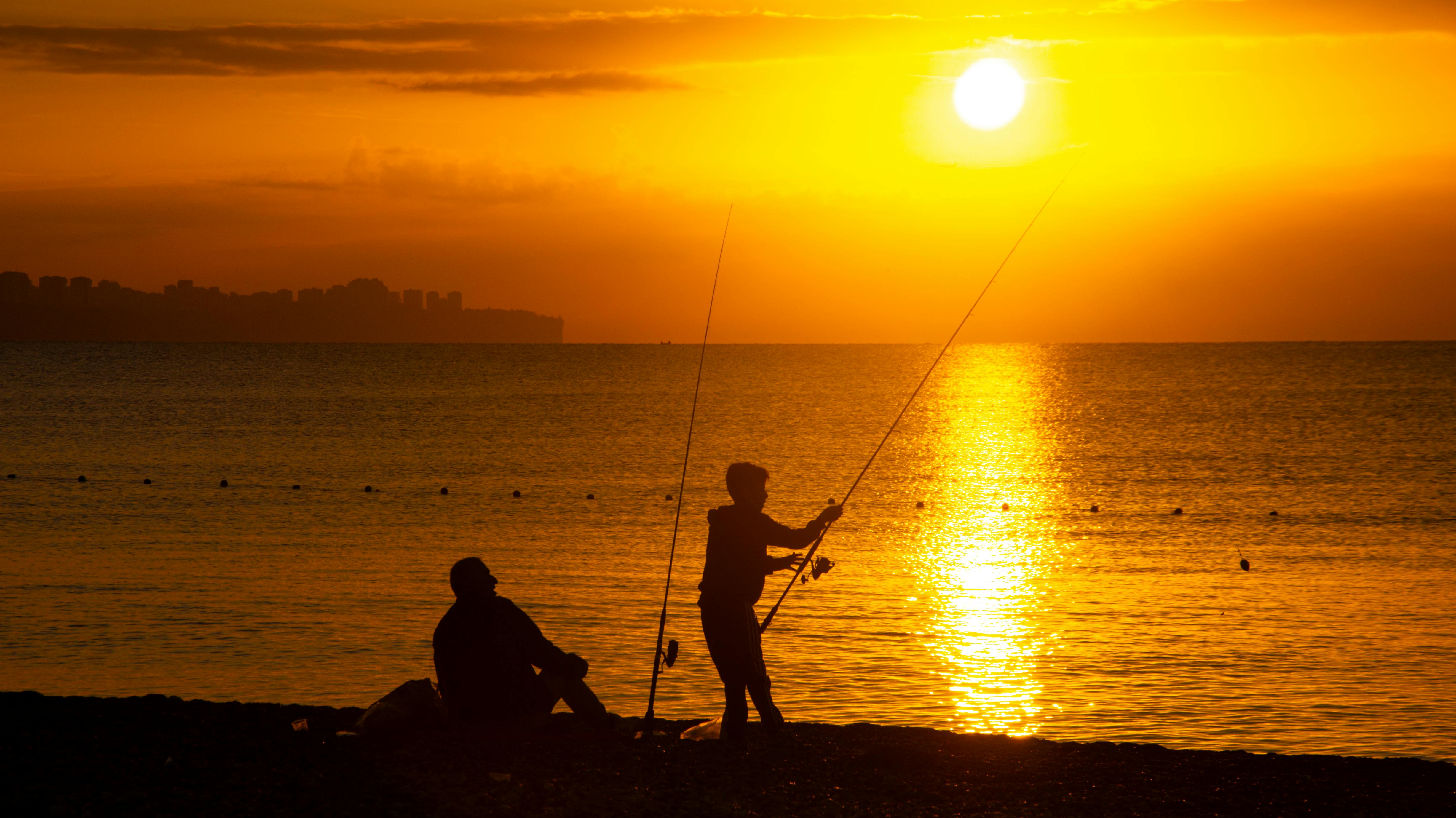 Two fishermen in silhouette with fishing rods on a beach at golden sunset.