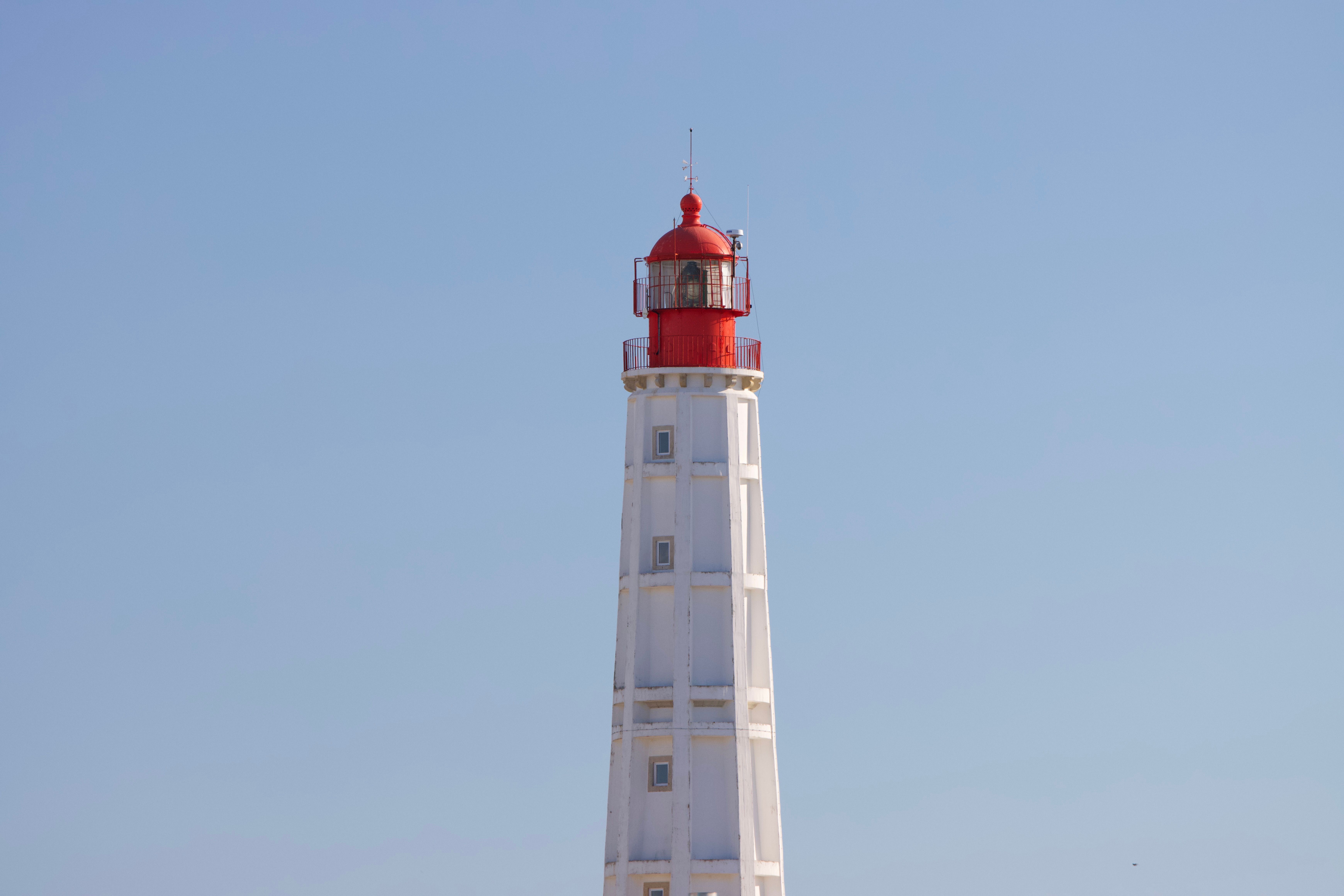 Stunning image of the iconic red-top white lighthouse under a clear blue sky in Faro, Portugal. - Faro
