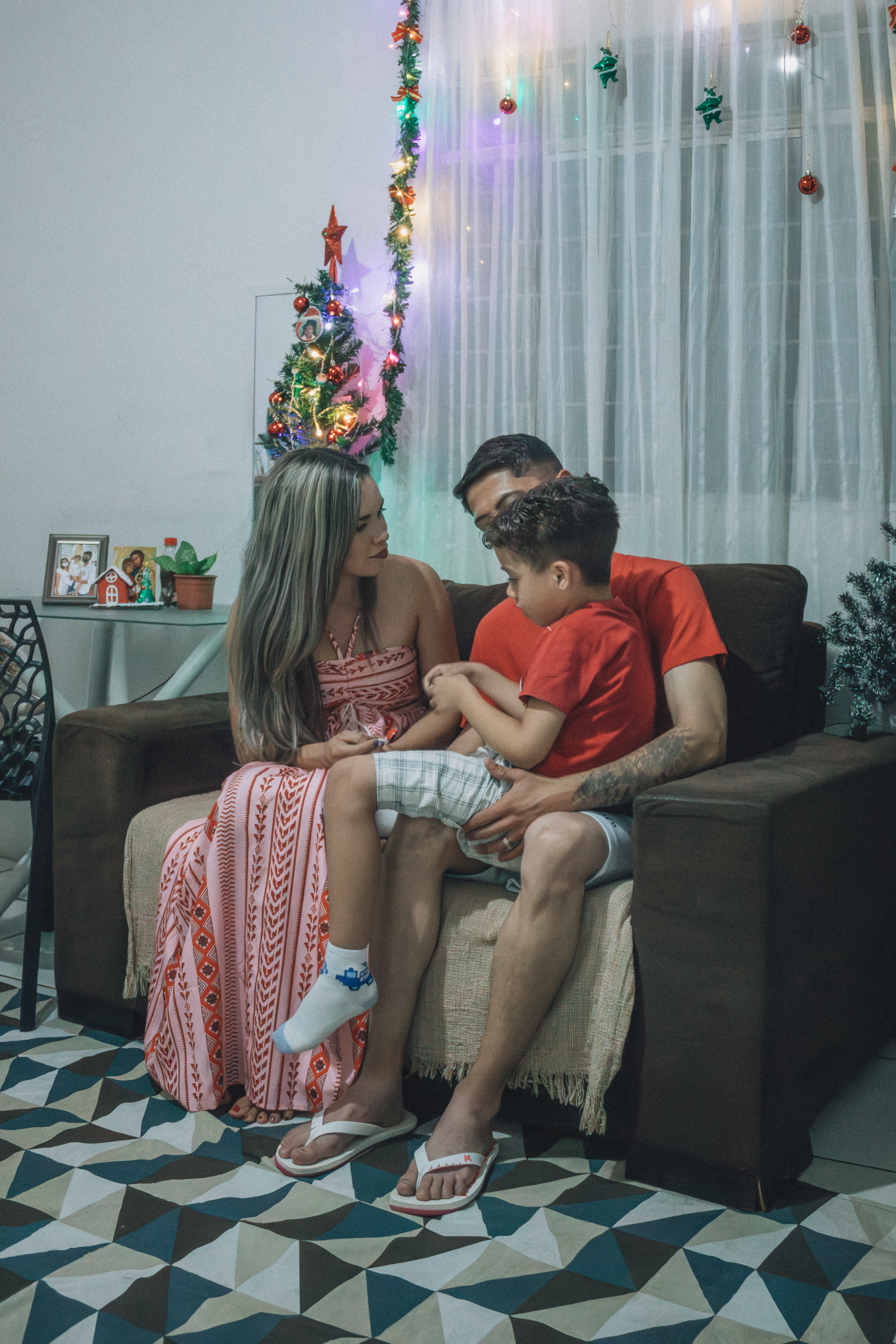 A family of three enjoys a cozy Christmas evening indoors with a decorated tree.