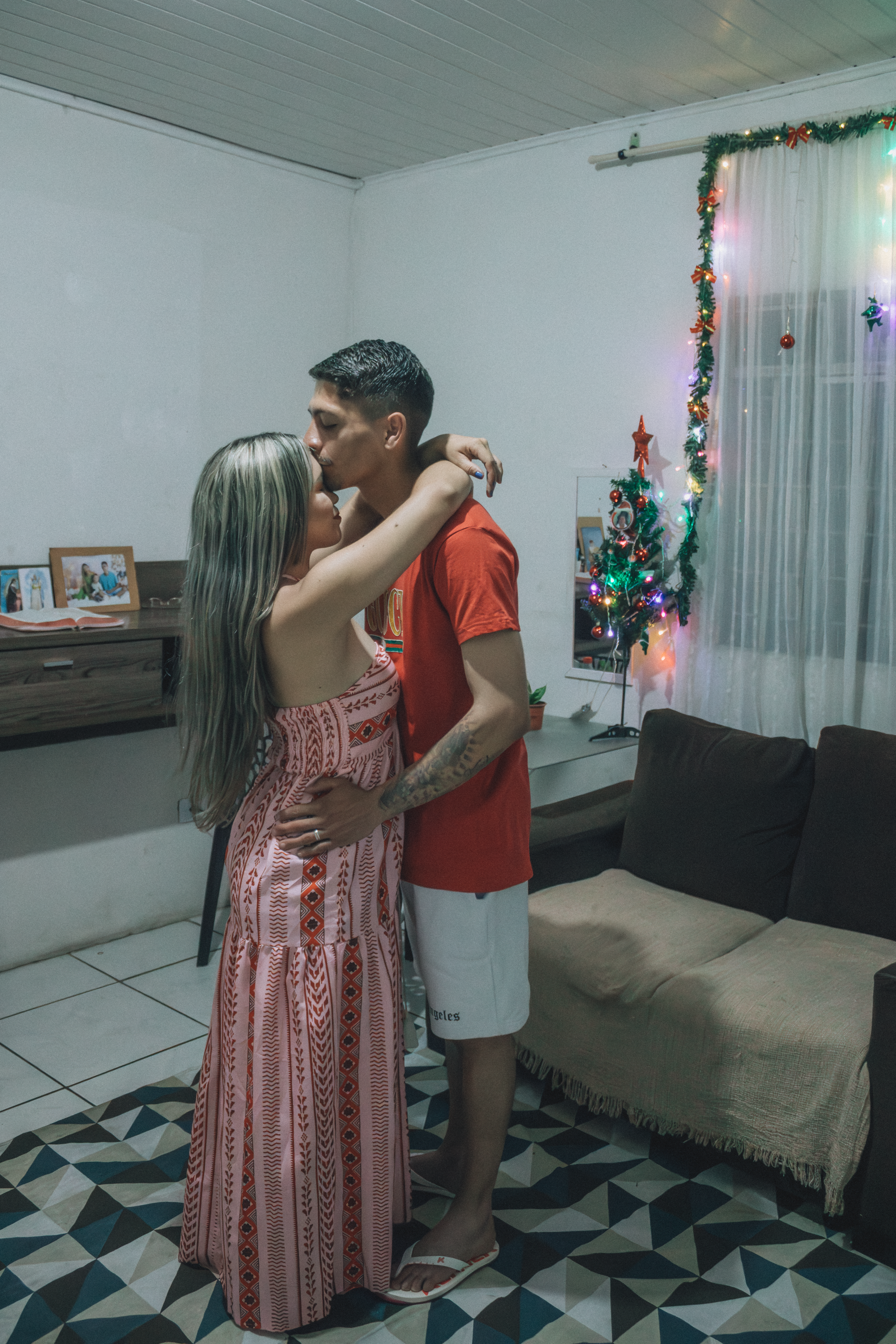 A couple sharing an affectionate moment near a Christmas tree inside a cozy room.