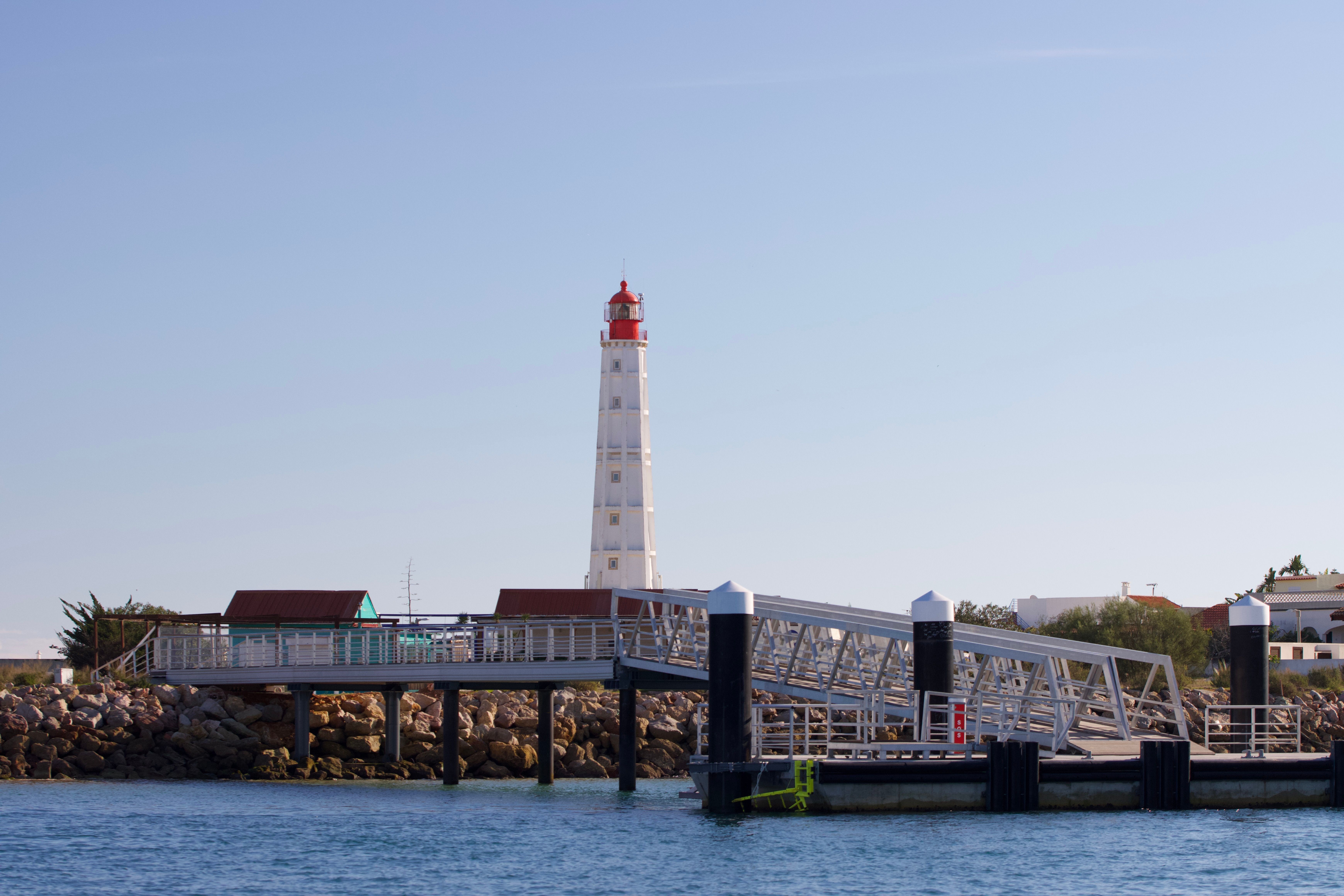 Beautiful scene of the Farol Island Lighthouse at the coastline in Faro, Portugal, during a clear summer day.