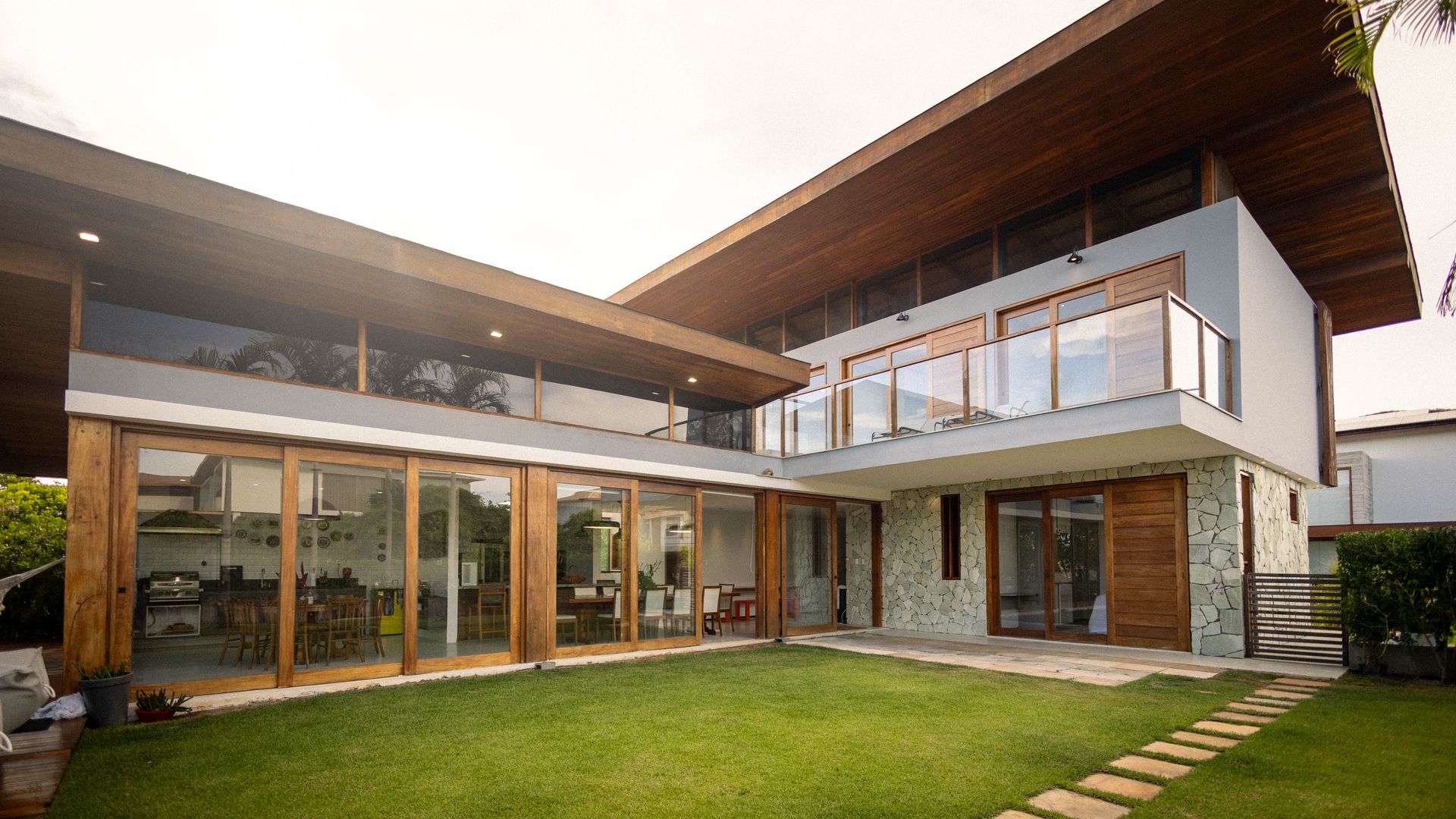 Luxury modern house exterior with floor-to-ceiling glass windows and wooden finish, green lawn