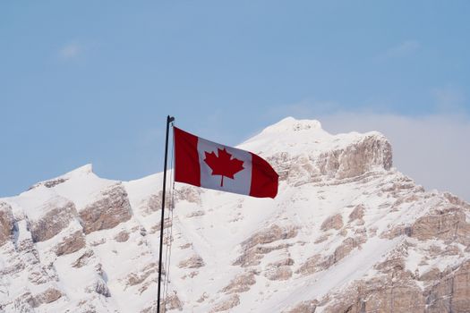 Canadian flag waving in front of snow-covered mountains in Banff National Park, Alberta.