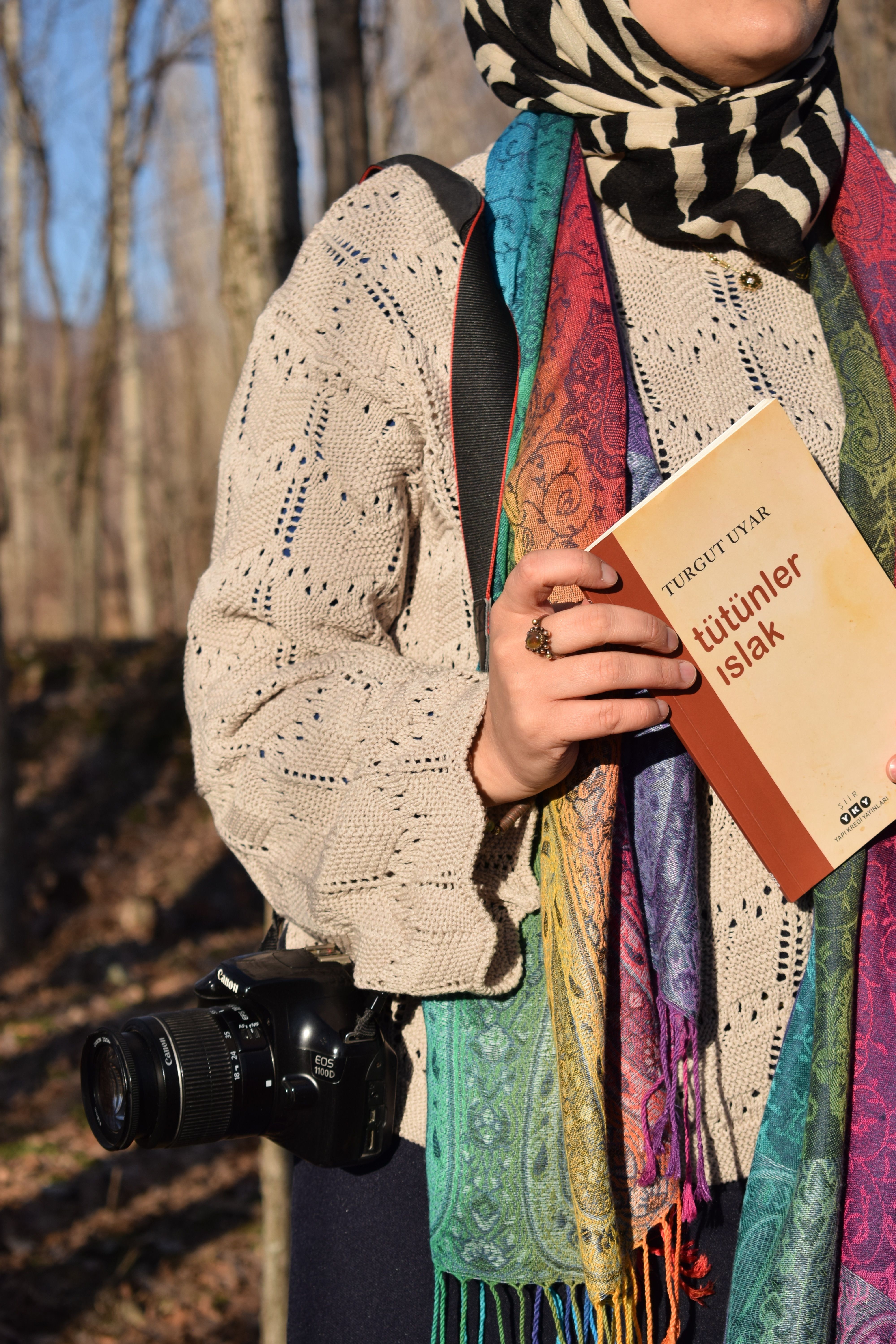 Woman holding a Turgut Uyar book outdoors, wearing vibrant scarf.