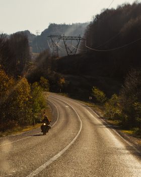 Lone motorcyclist riding through a scenic autumn landscape on a winding road.