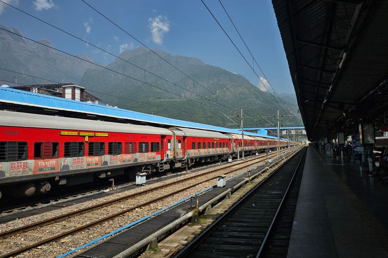 A vibrant red train at an outdoor station with scenic mountain backdrop, ideal for travel themes.