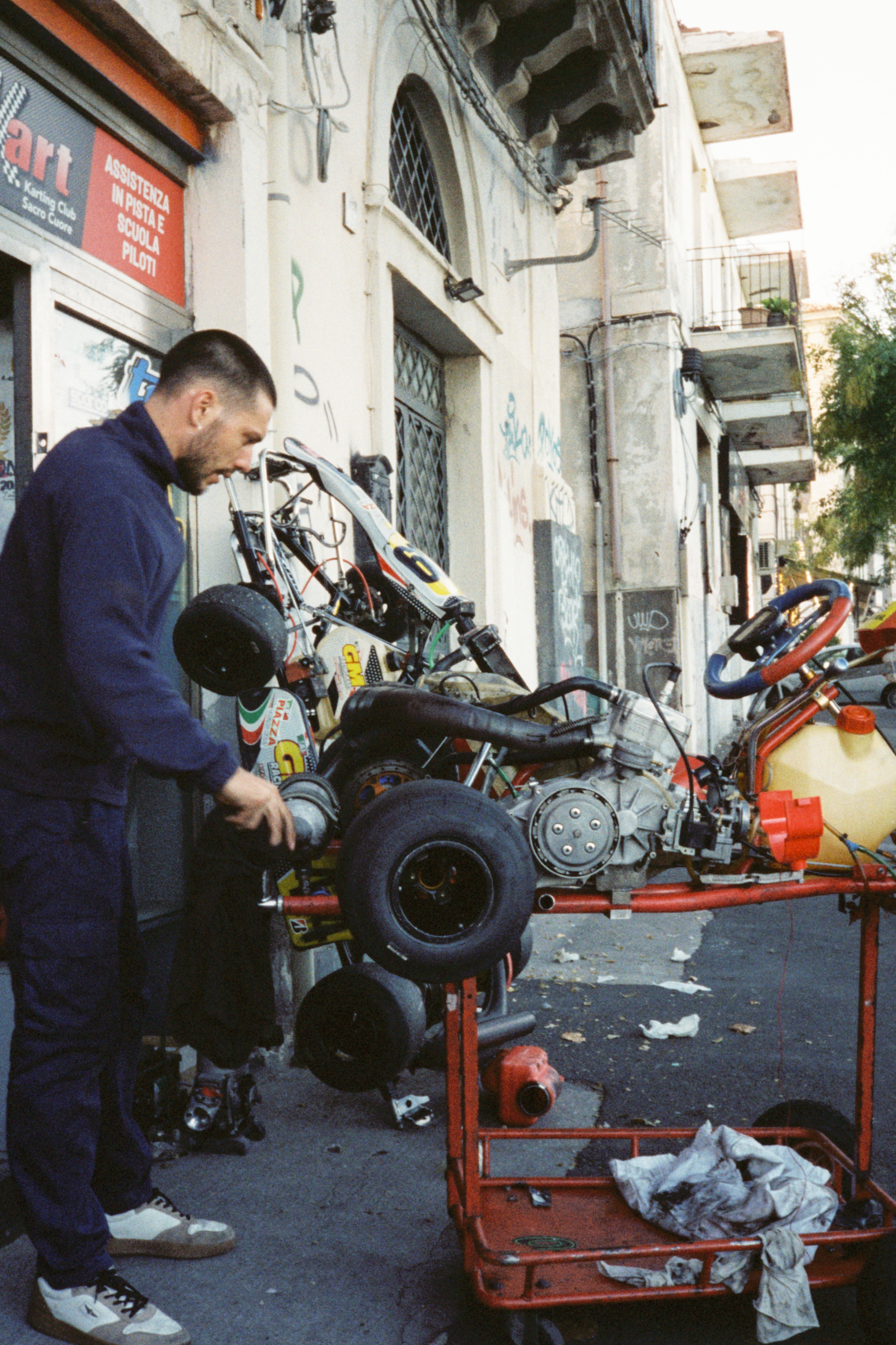 A mechanic working on a go-kart outdoors in Sicily, Italy, showcasing vintage street art.