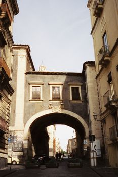 Explore the historic stone archway in Catania, Sicily, capturing classic architecture and vibrant street life.