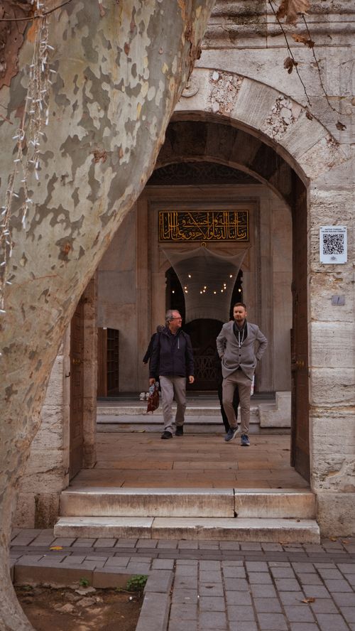 Free Two men walk through an ancient stone archway, showcasing intricate design. Stock Photo