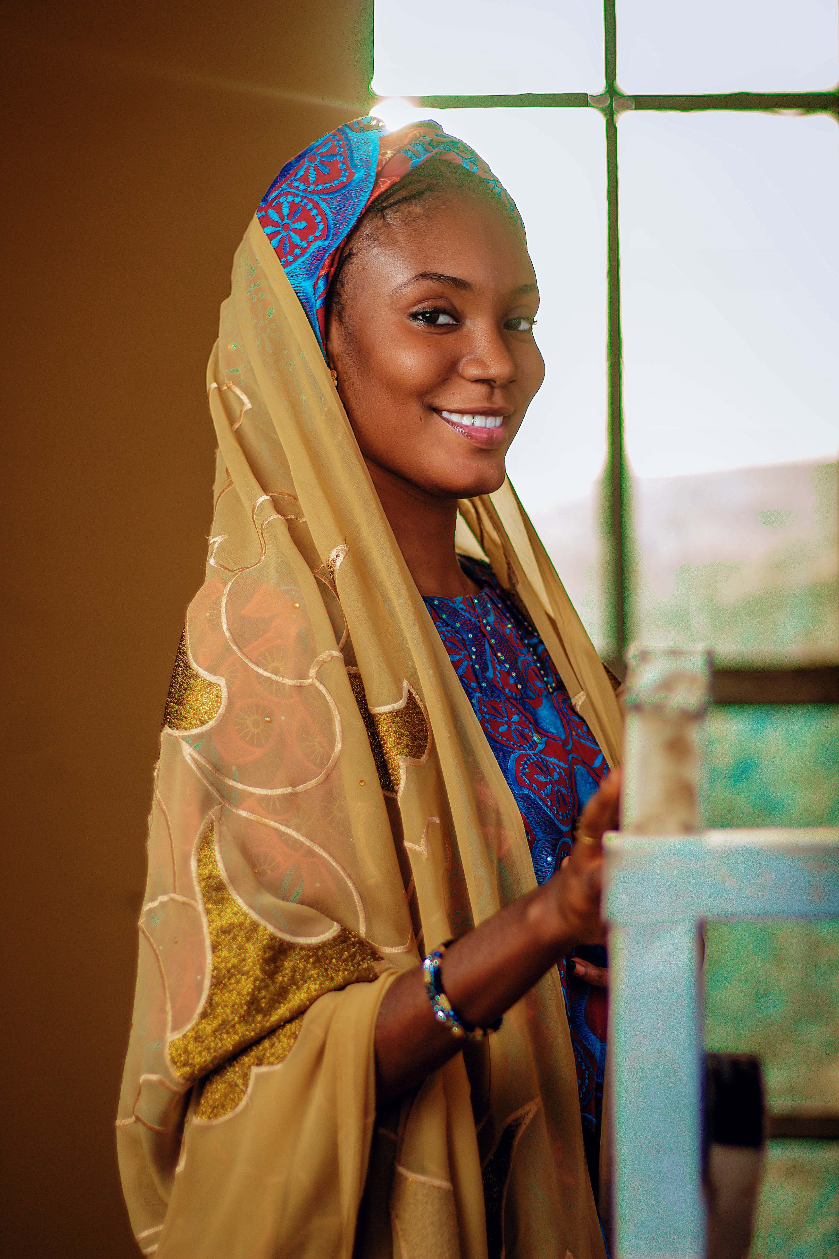 Portrait of a woman in vibrant traditional attire, captured in natural light by a window.