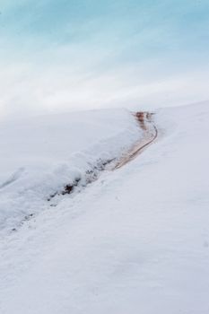 A serene snow-covered path meandering through a vast, white winter landscape under a clear sky.