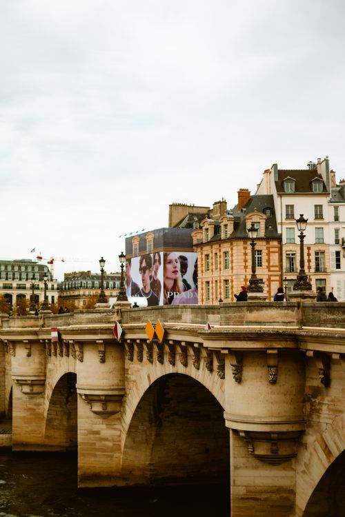 Free Capture of a historic bridge in Paris featuring a fashion billboard under cloudy skies. Stock Photo