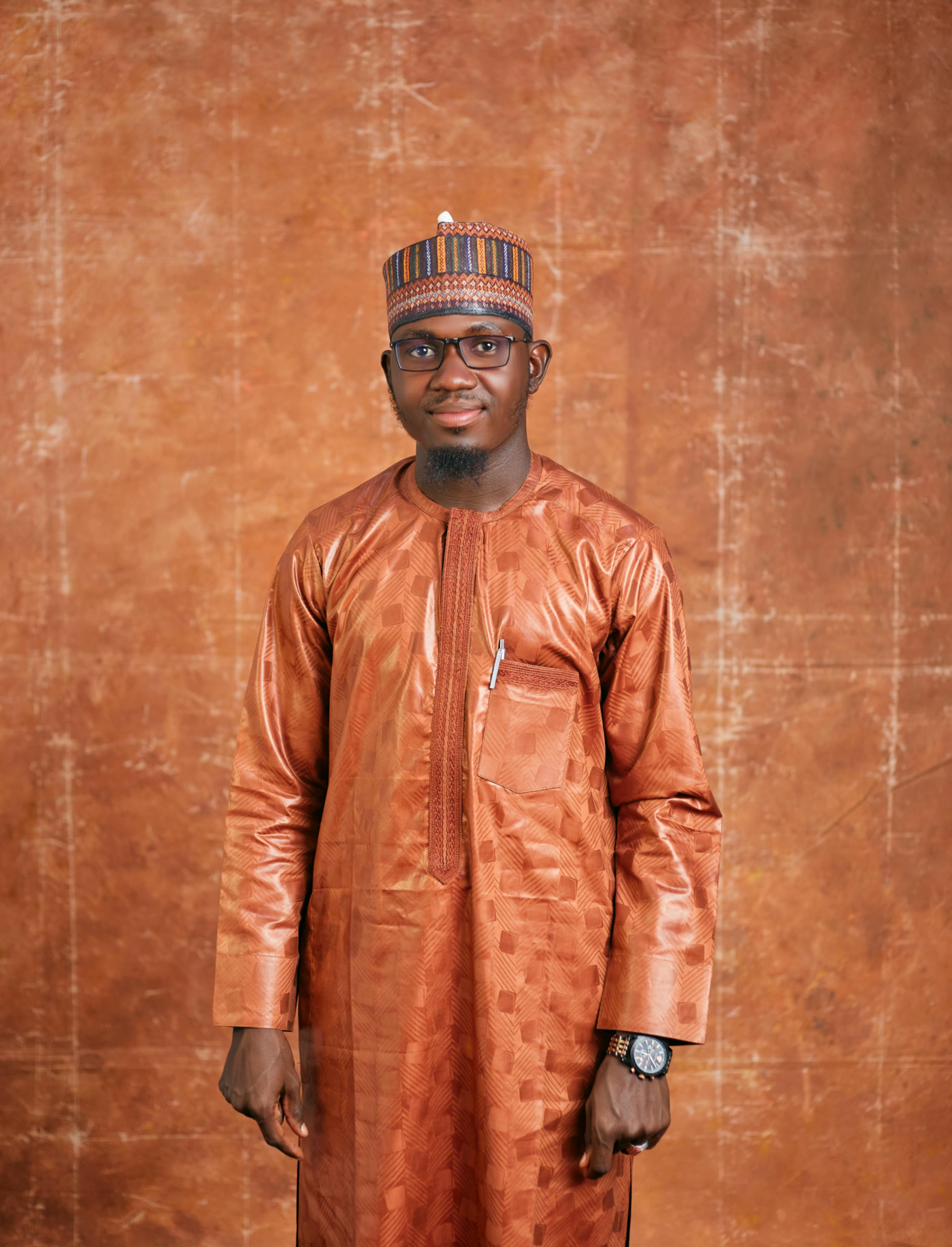 A confident man wearing traditional African clothing standing against a textured background.