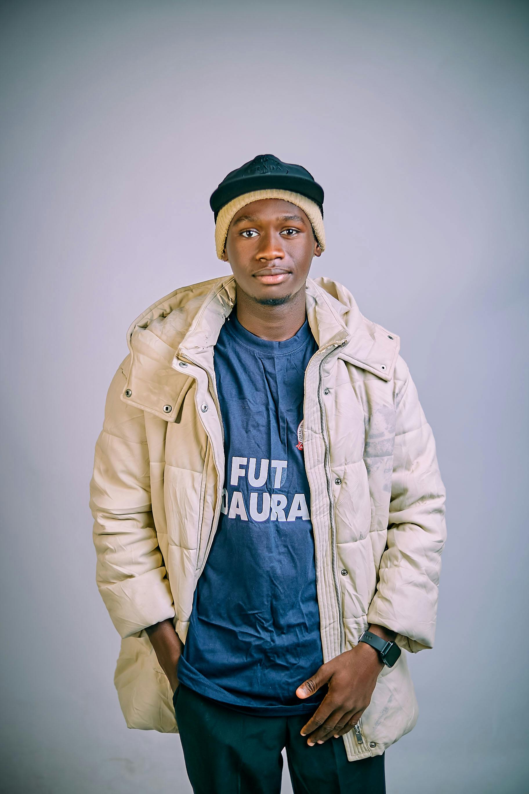 Portrait of a young man wearing a beige winter jacket and black beanie against a neutral background.