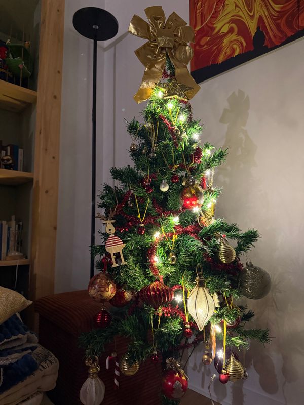 Petit sapin de Noël avec guirlande lumineuse et nœud doré dans un coin de salon