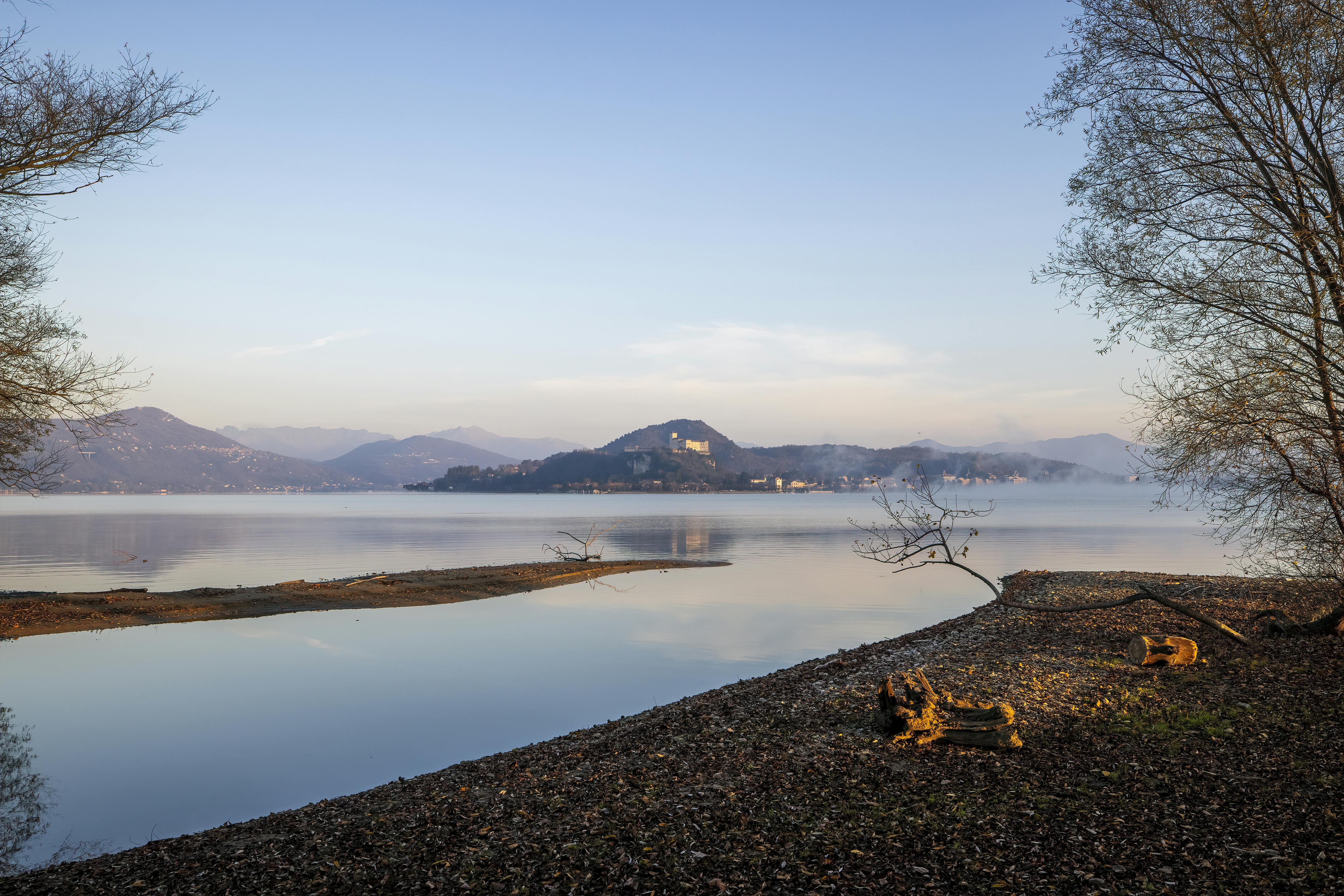 Peaceful lakeside landscape with mountains under a clear sunrise sky, ideal for nature enthusiasts.