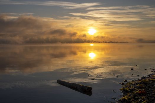 A serene sunrise over a tranquil lake with mist and reflections, capturing the peaceful morning atmosphere.