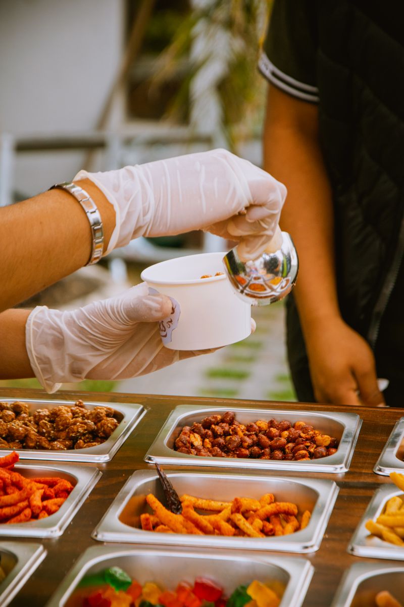 A close-up of a food stall attendant serving snacks into a bowl outdoors.