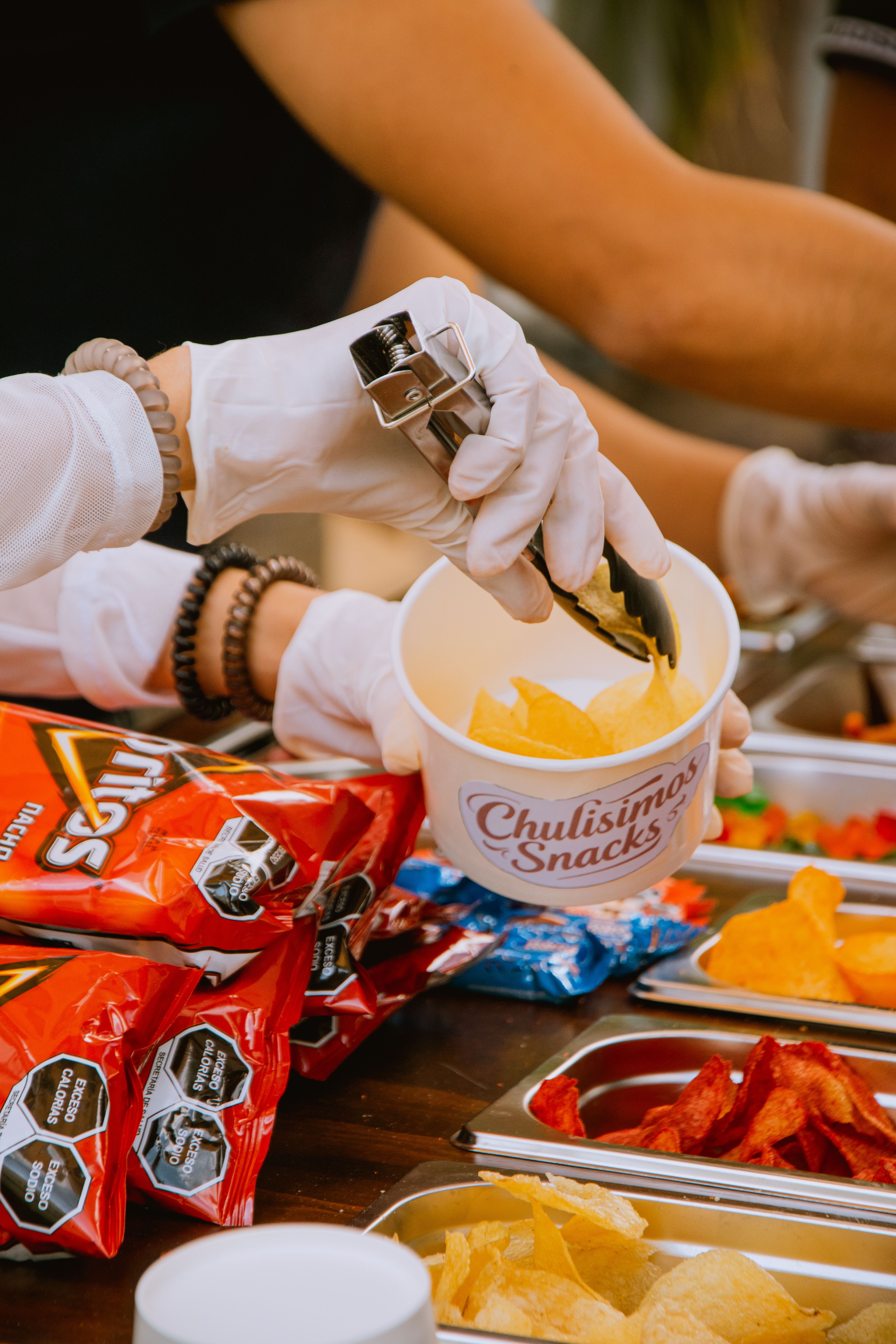 Hands serving assorted chips at an outdoor snack bar event.