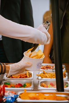 Image of a street food vendor serving fries from a variety of snacks outdoors.