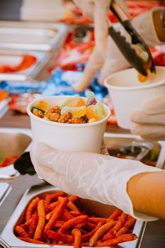 A street vendor carefully serving vibrant snacks into cups with tongs, displaying a variety of colorful treats.