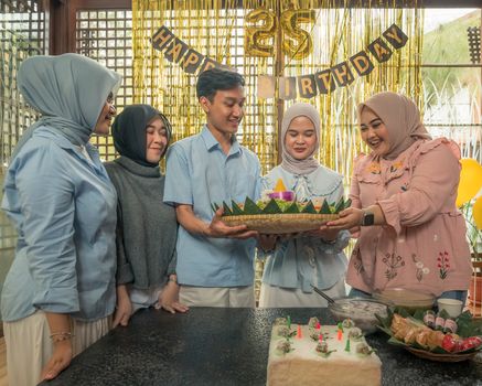 Friends celebrating a 25th birthday indoors in Jawa Barat with traditional Tumpeng dish.
