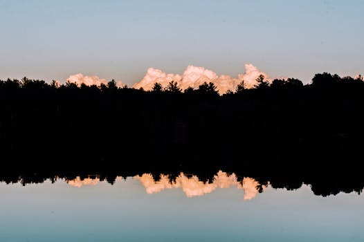 日落时分，树木映衬着云层的宁静轮廓倒映在湖面上