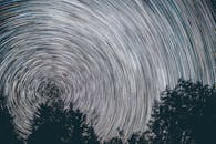 夜晚，迷人的星轨在树木的轮廓上勾勒出引人注目的螺旋图案