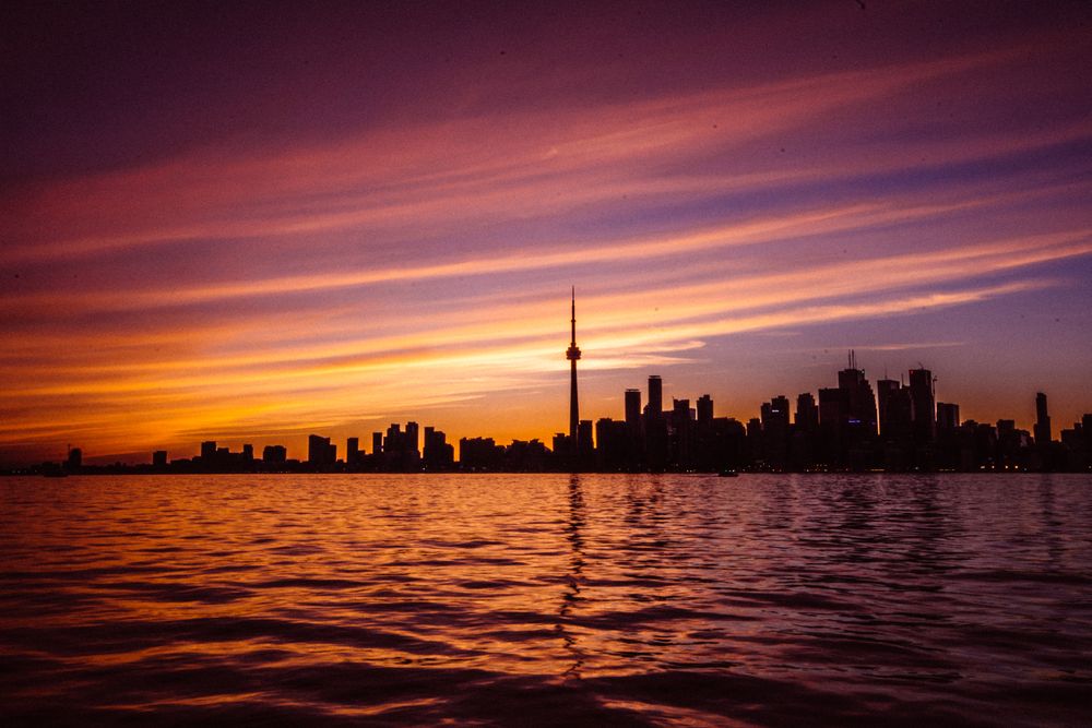 Capture of Toronto's skyline with vibrant sunset colors reflecting on the water, featuring the iconic CN Tower.