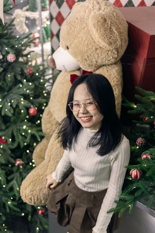 Free A young woman smiling beside a large teddy bear and Christmas decorations. Stock Photo