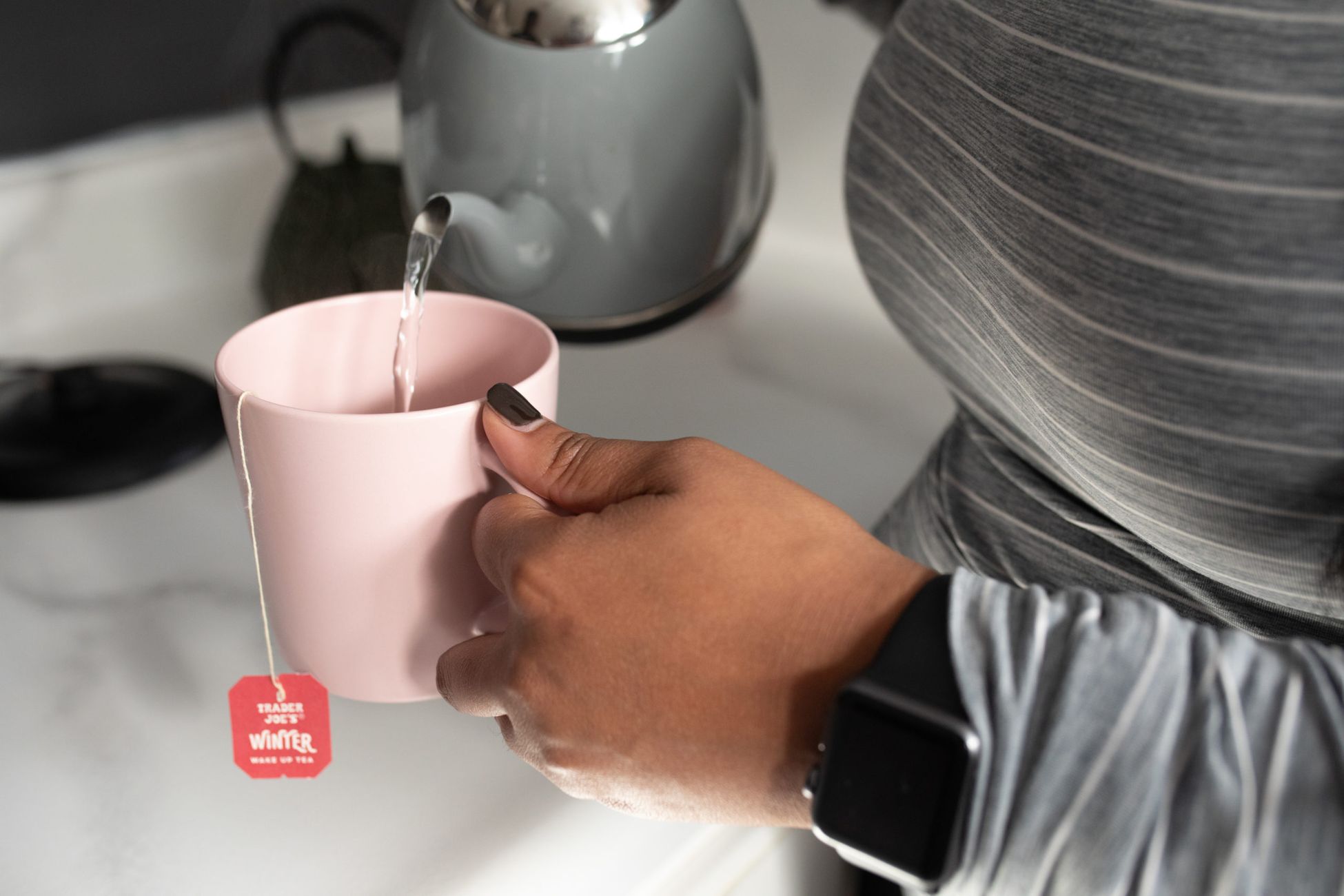 Person pouring tea into a pink mug with a winter-themed tea bag.