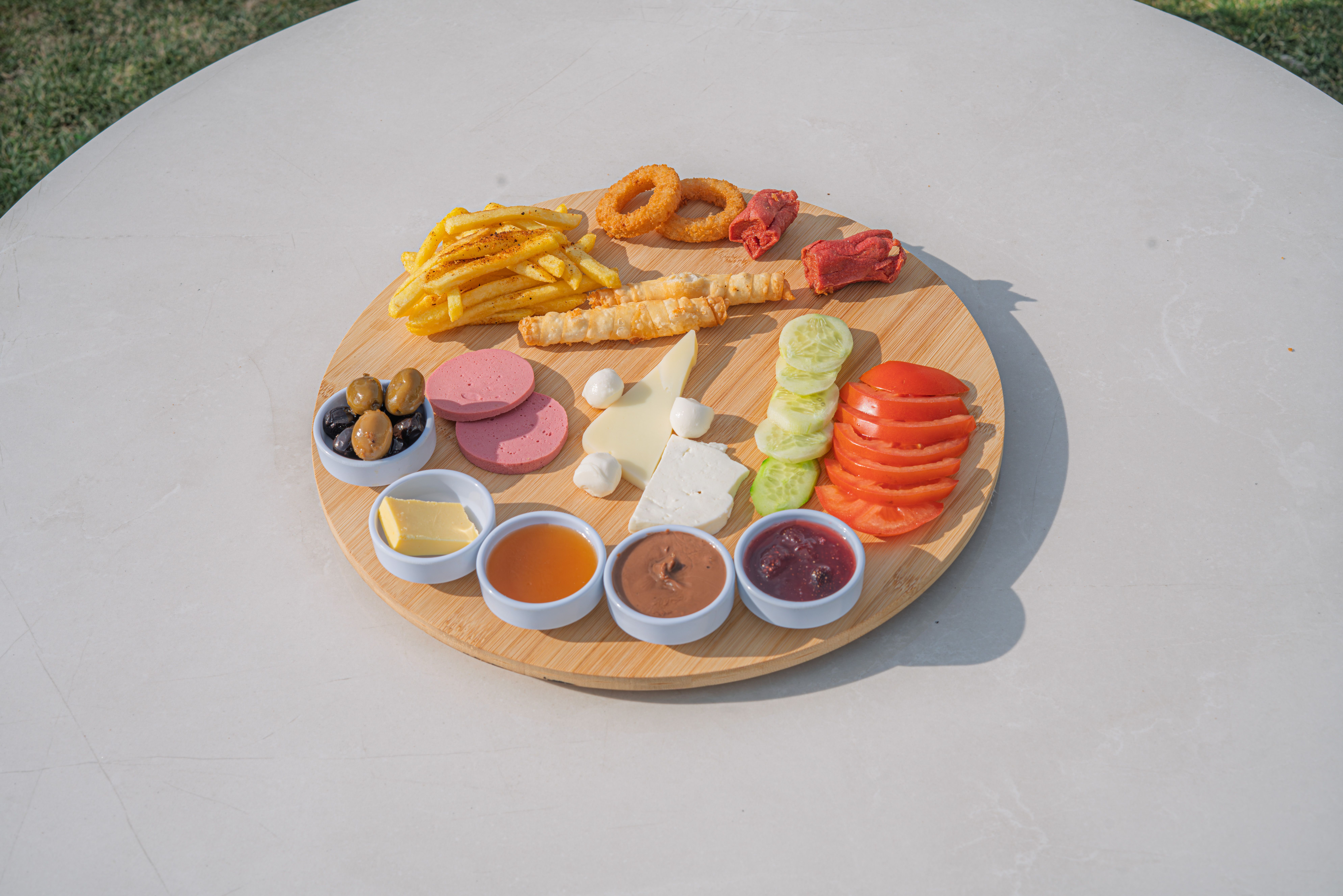 A vibrant Turkish breakfast platter with assorted foods served on a wooden board outdoors.