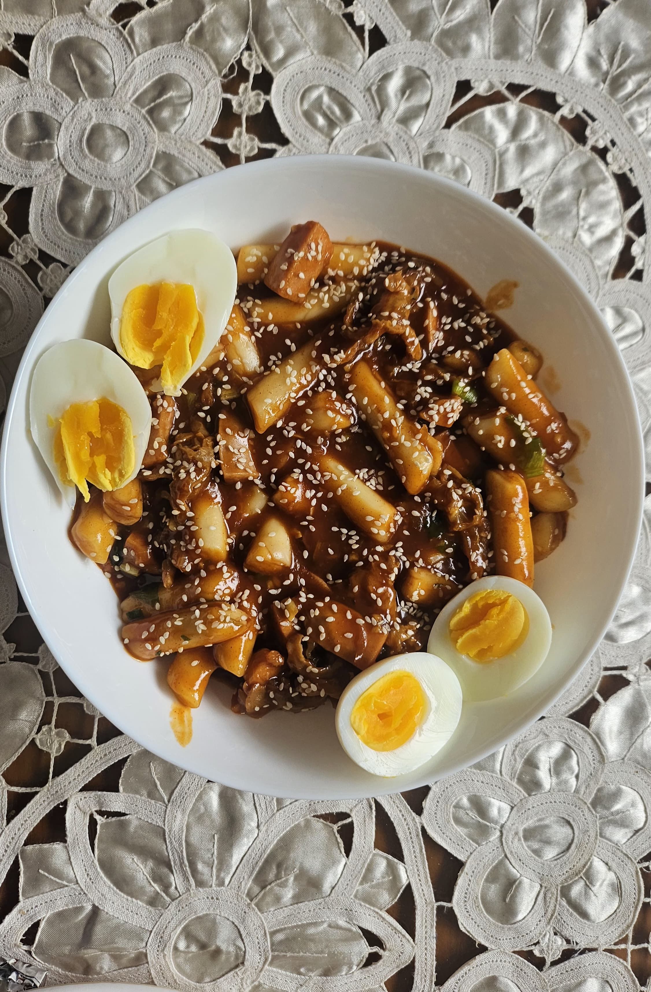 Steaming bowl of glossy red Korean rice cakes in spicy gochujang sauce, topped with fresh scallions and sesame seeds