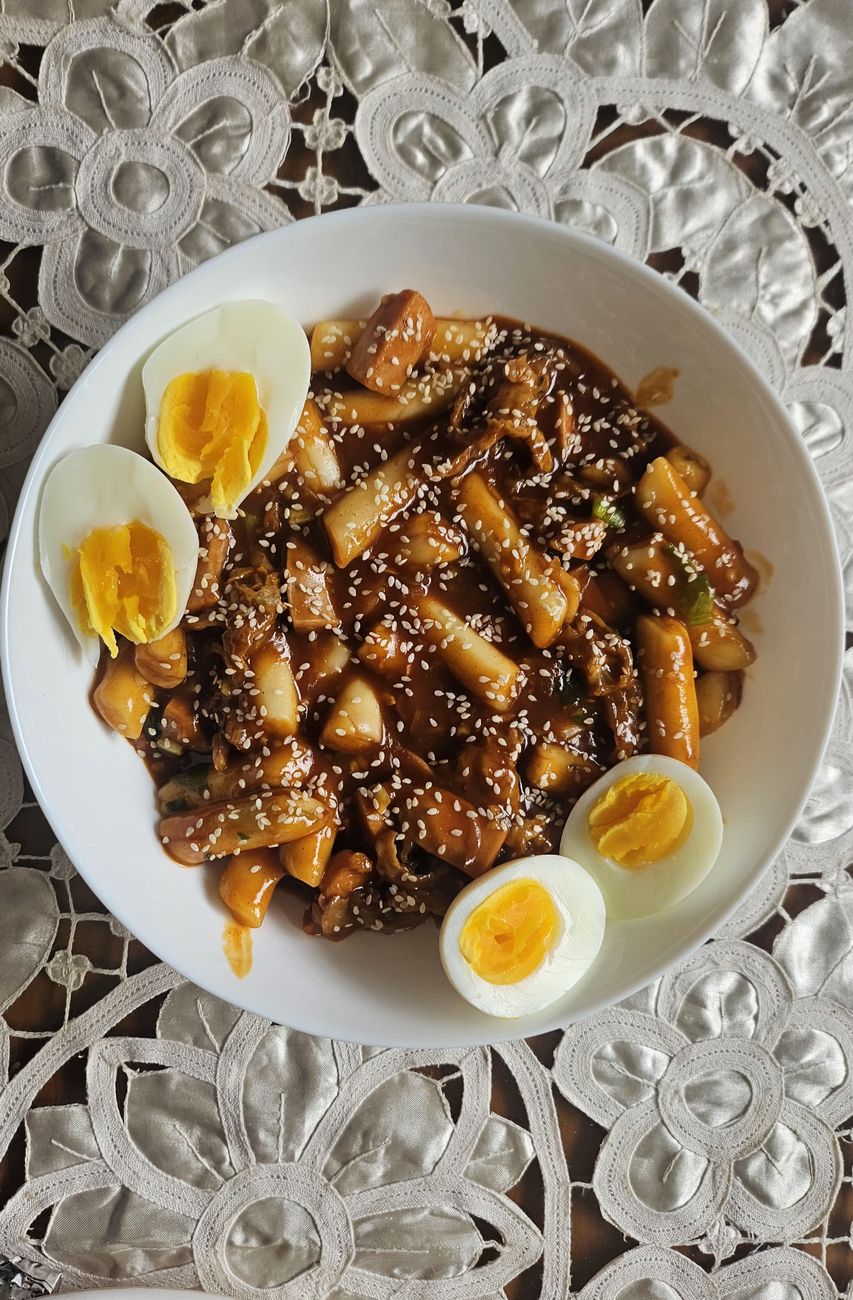 Steaming bowl of glossy red Korean rice cakes in spicy gochujang sauce, topped with fresh scallions and sesame seeds