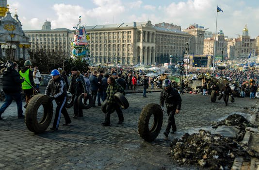 Grande folla in Piazza Indipendenza a Kiev con operai che trasportano pneumatici, scena vivace.