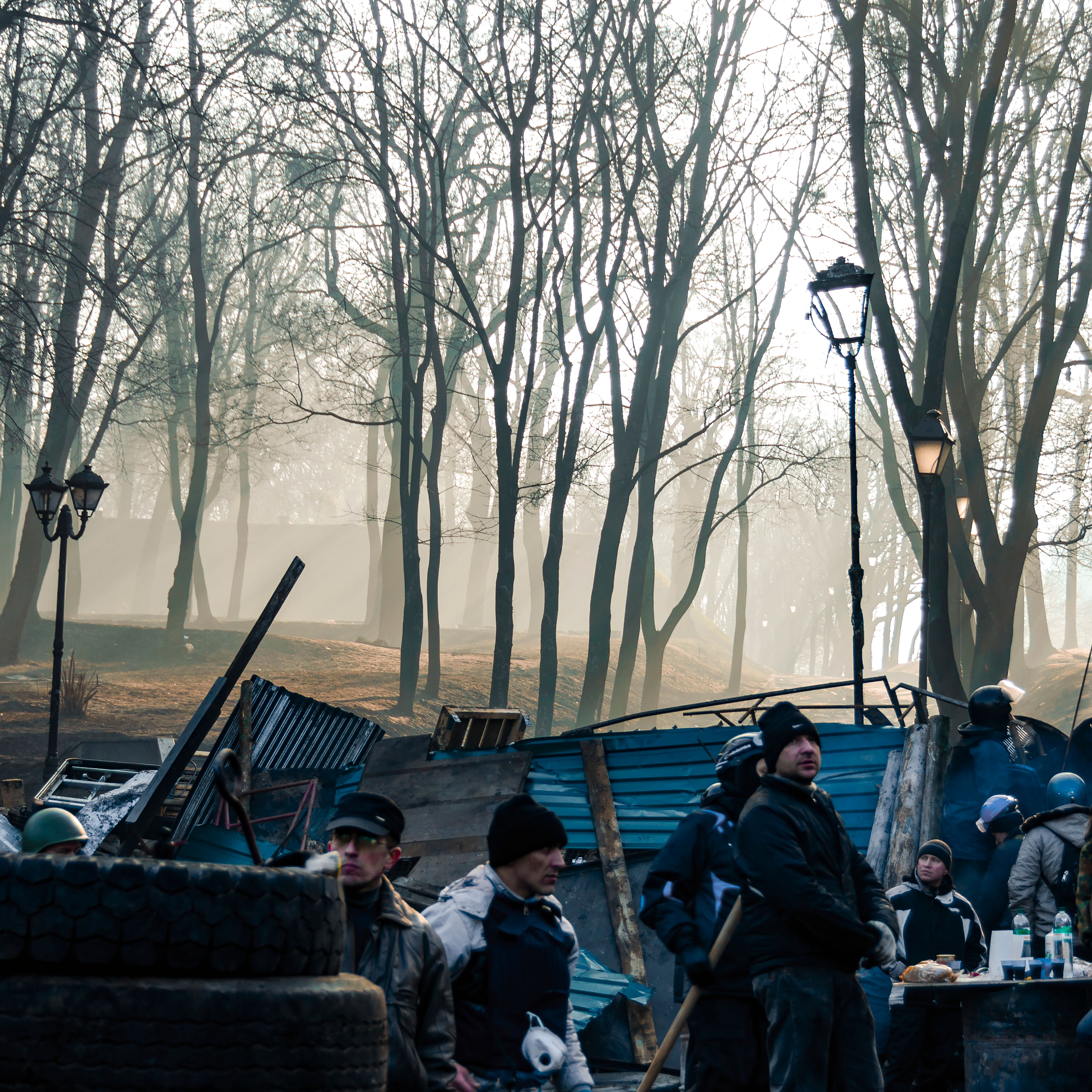 Dawn in a Kyiv park with people amidst improvised barricades and trees.