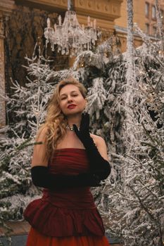 Glamorous woman in a red dress poses elegantly among snow-covered trees, exuding winter elegance.