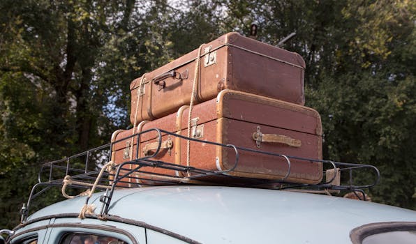 Stack of vintage suitcases secured on a classic car roof rack for an outdoor road trip.