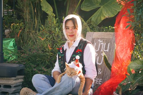 Free A cheerful woman holding a cat dressed in a festive outfit, surrounded by lush greenery outdoors. Stock Photo