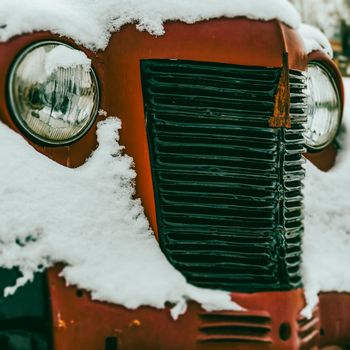 Close-up of a vintage truck covered in snow, showcasing its headlamps and grille in a wintery setting in Lviv, Ukraine.