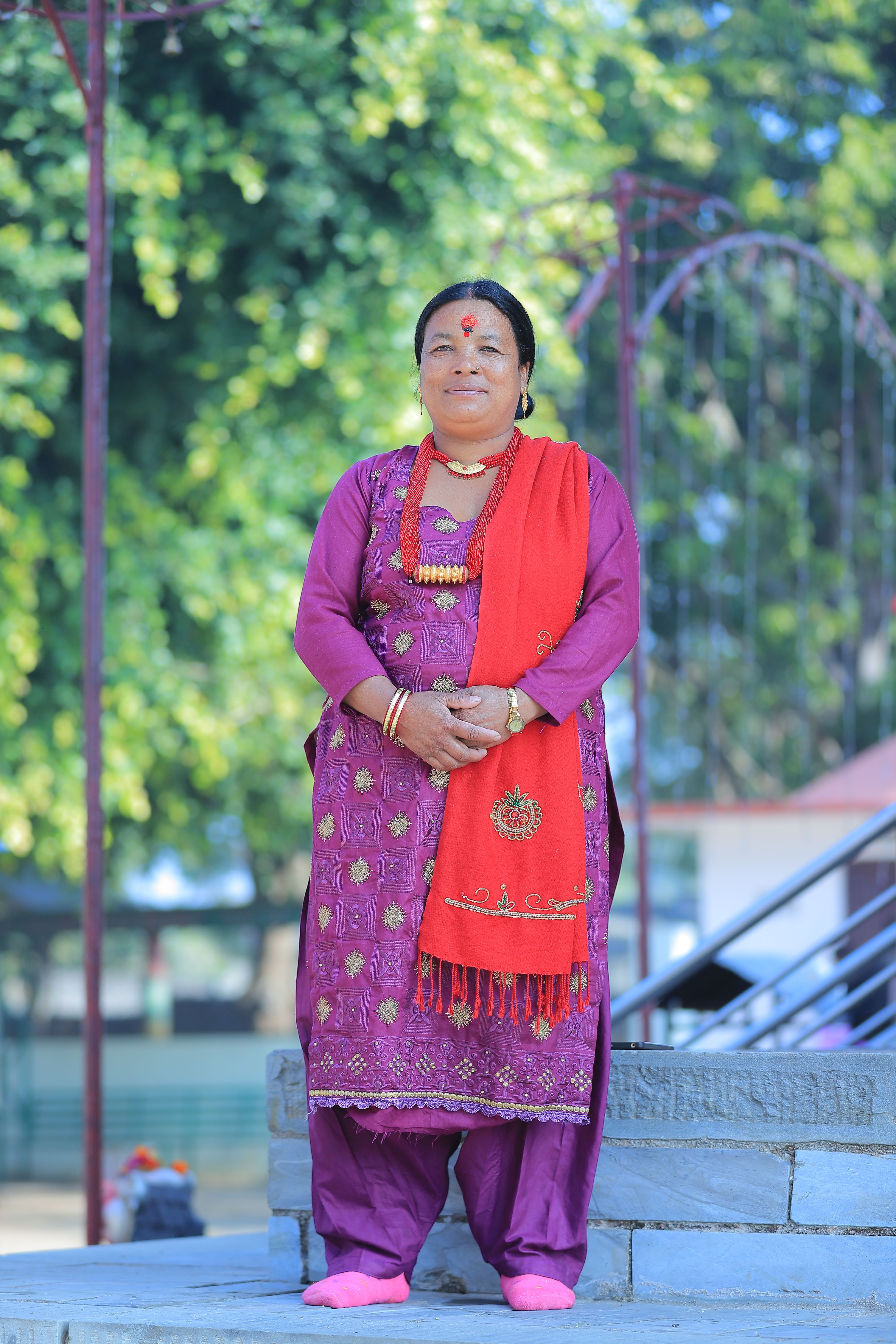 Smiling woman in vibrant traditional dress outdoors with green background.