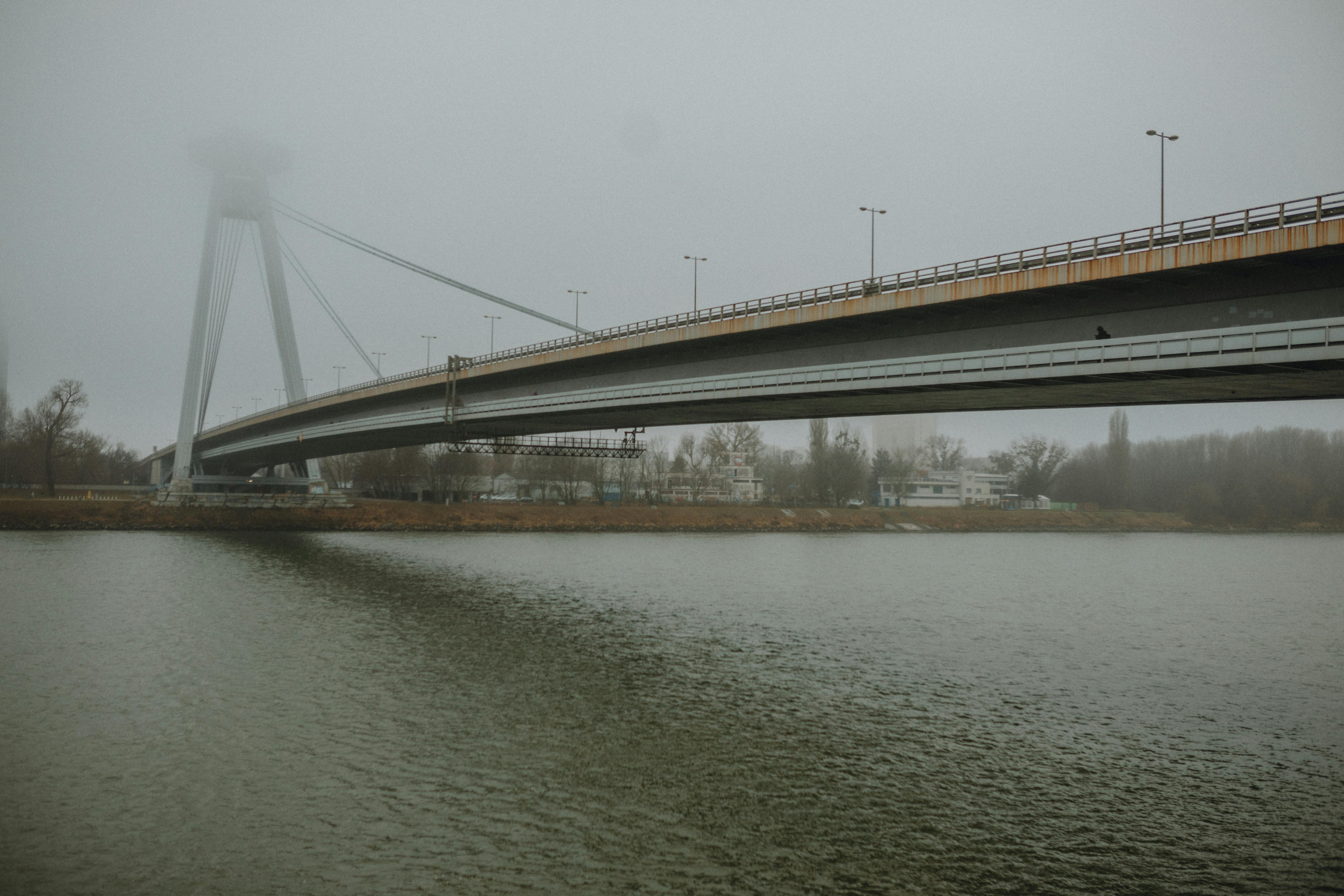 A misty morning view of the UFO Bridge in Bratislava, reflecting over the calm river.