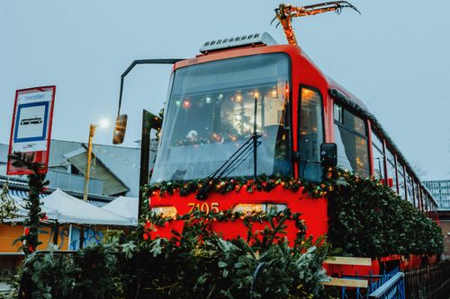 Free A red tram beautifully decorated with evergreen garlands and Christmas lights, evoking holiday cheer. Stock Photo