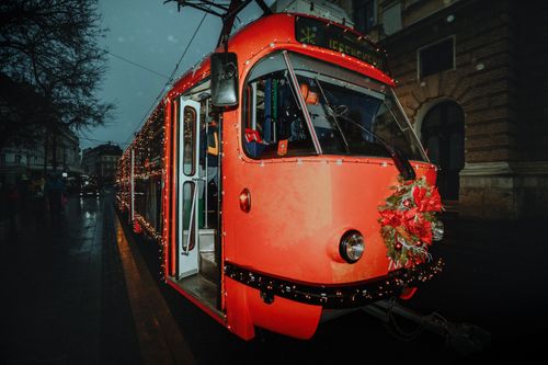 Free A bright red tram adorned with Christmas lights and wreath, captured on a rainy evening. Stock Photo