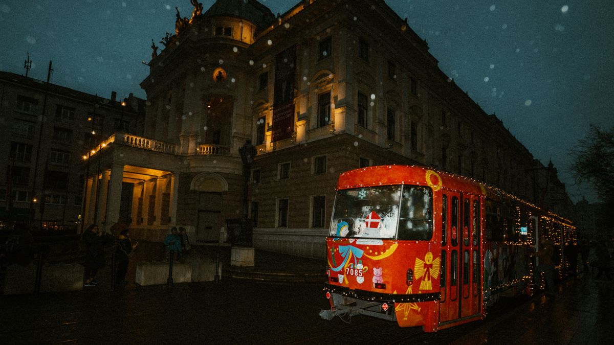 A decorated red tram on a snowy night by a historic building, creating a festive atmosphere.