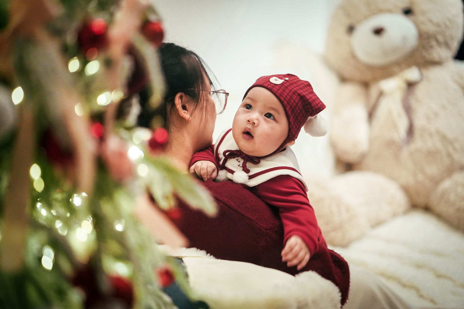 Cute baby with mother embracing holiday spirit near Christmas tree in cozy setting.